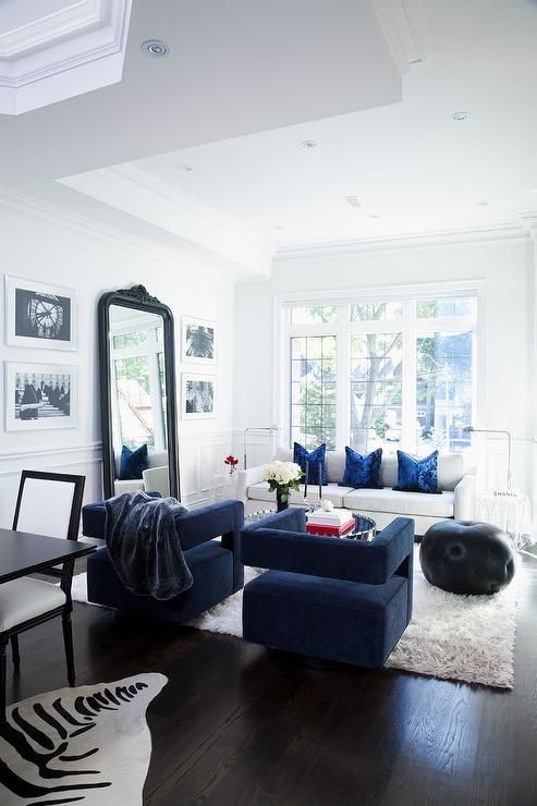 Elegant white and blue living room boasts blue velvet chairs .