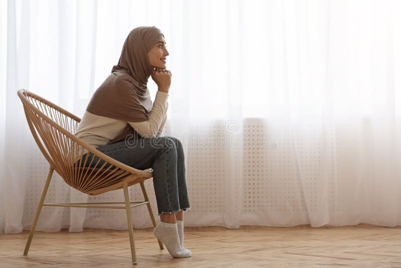 Muslim Girl in Hijab Relaxing in Wicker Chair at Home Stock Photo .
