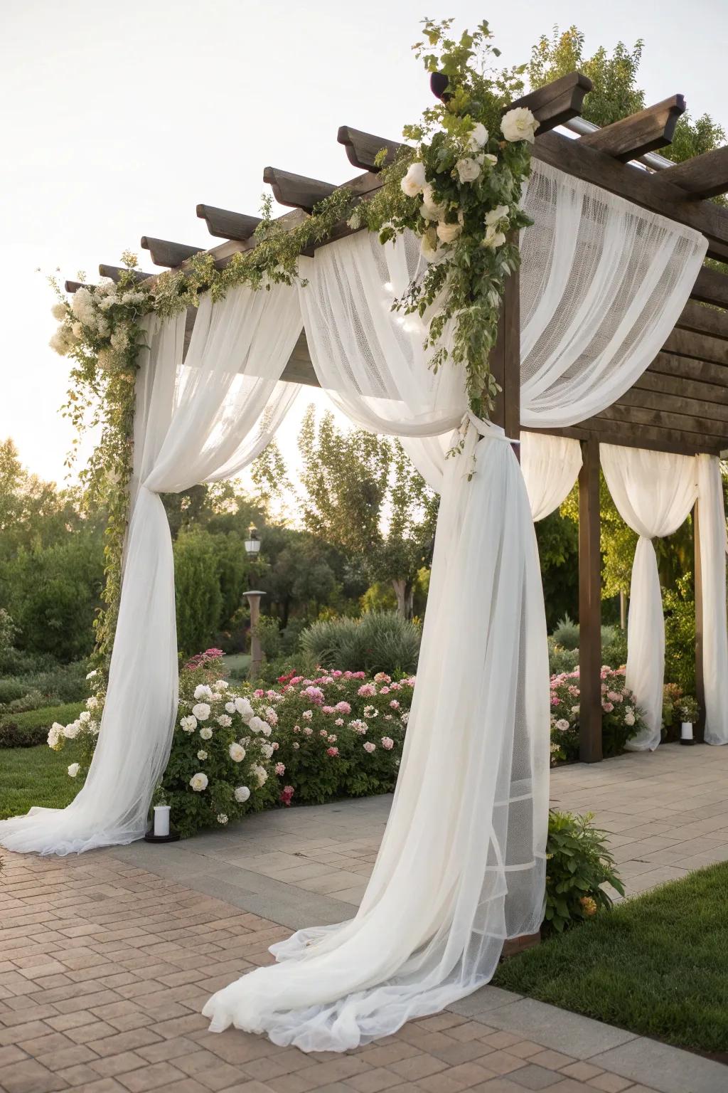 A wedding pergola elegantly draped with white chiffon fabric.