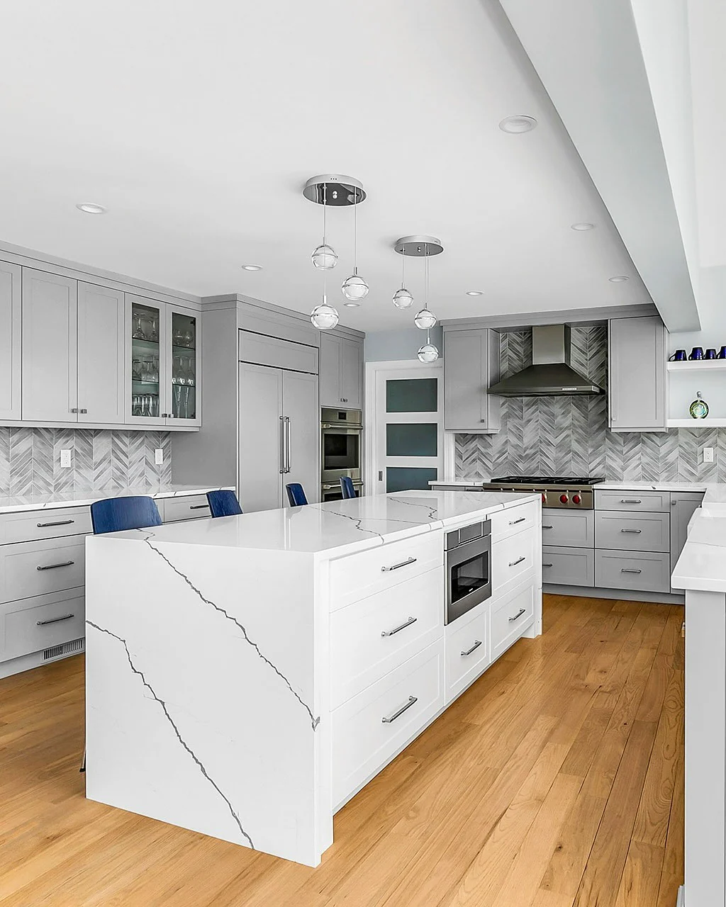 12. Herringbone Gray Elegance with Waterfall Island (Gray Kitchen Backsplash Ideas)