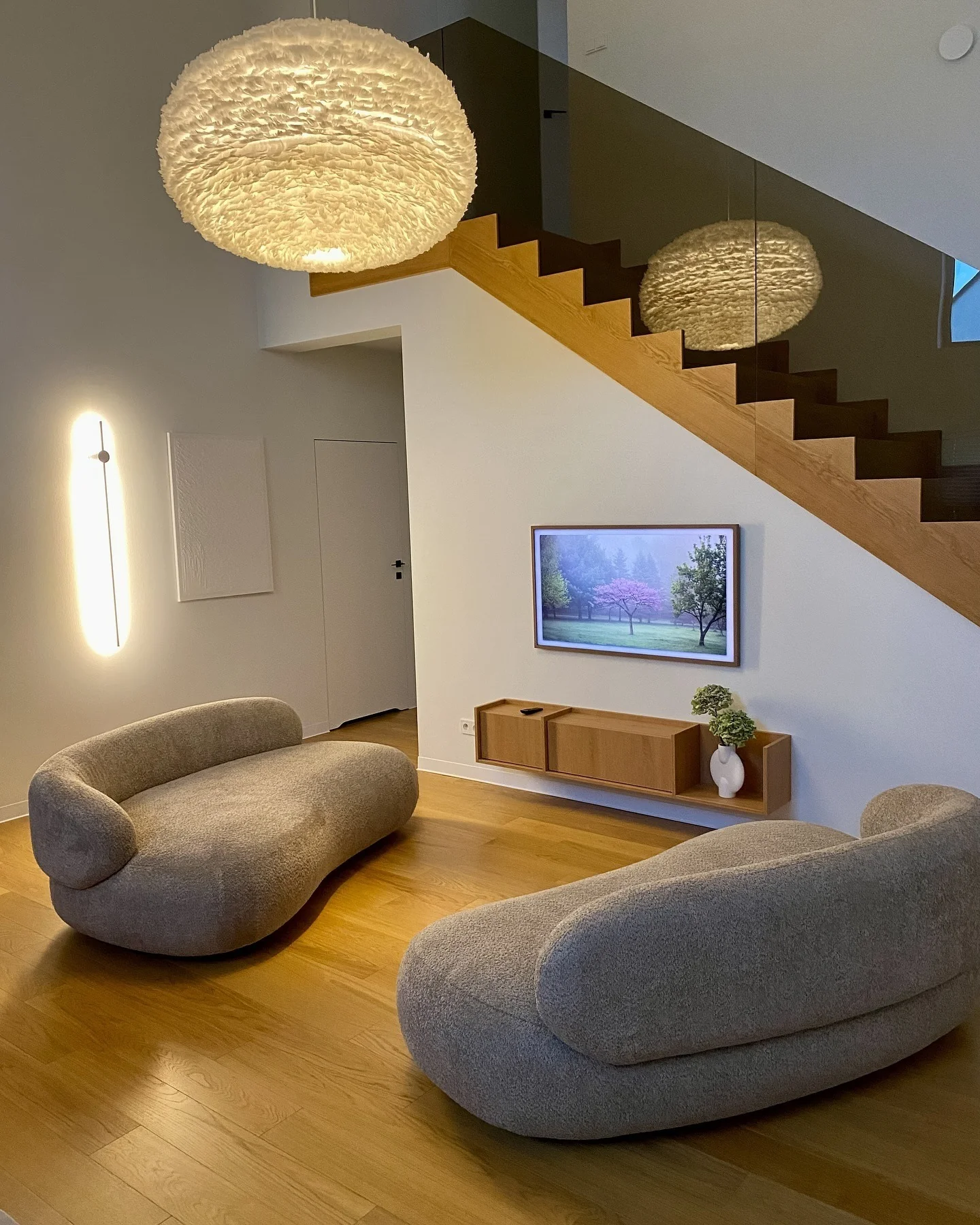 2. Sculptural Taupe Seating with Honeyed Wood Staircase (Japandi Living Room Ideas)